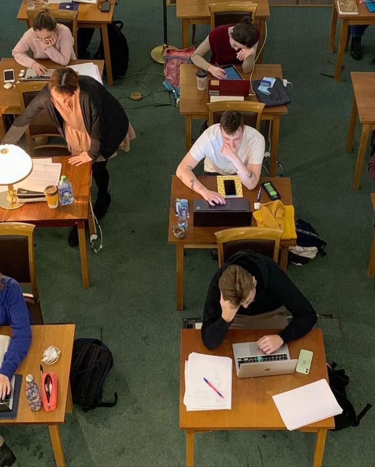 This may contain: several people are sitting at desks with laptops