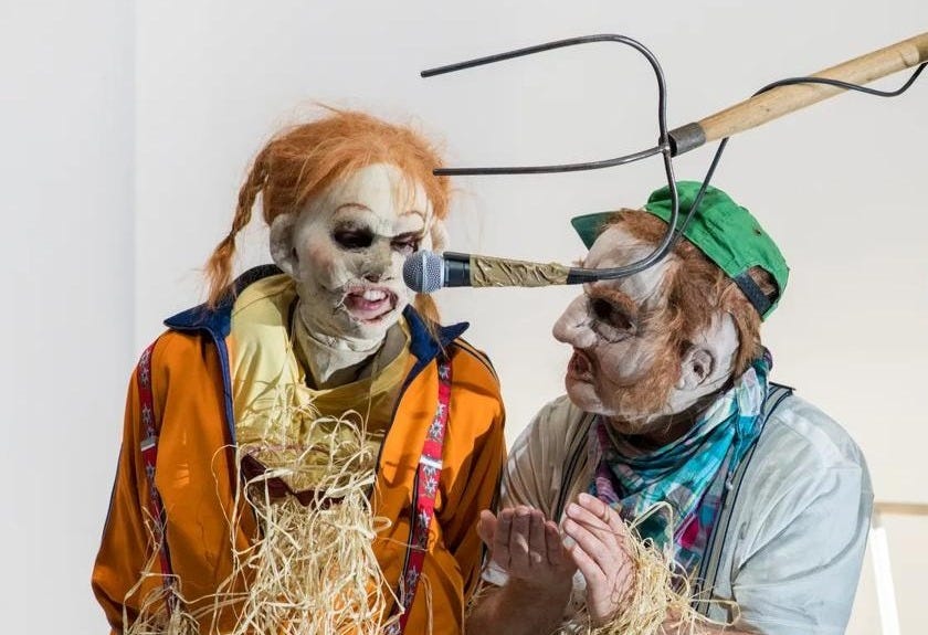 Three performers in scarecrow outfits, one is holding a pitchfork with a microphone attached over the other two's heads