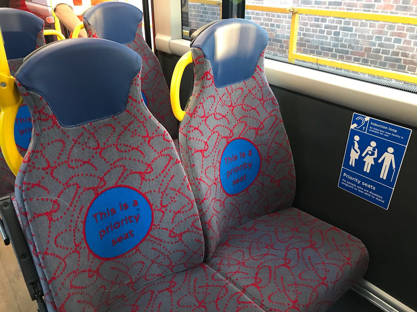 Photo of two priority seats on bus with "This is a priority seat." on the seat pattern.
