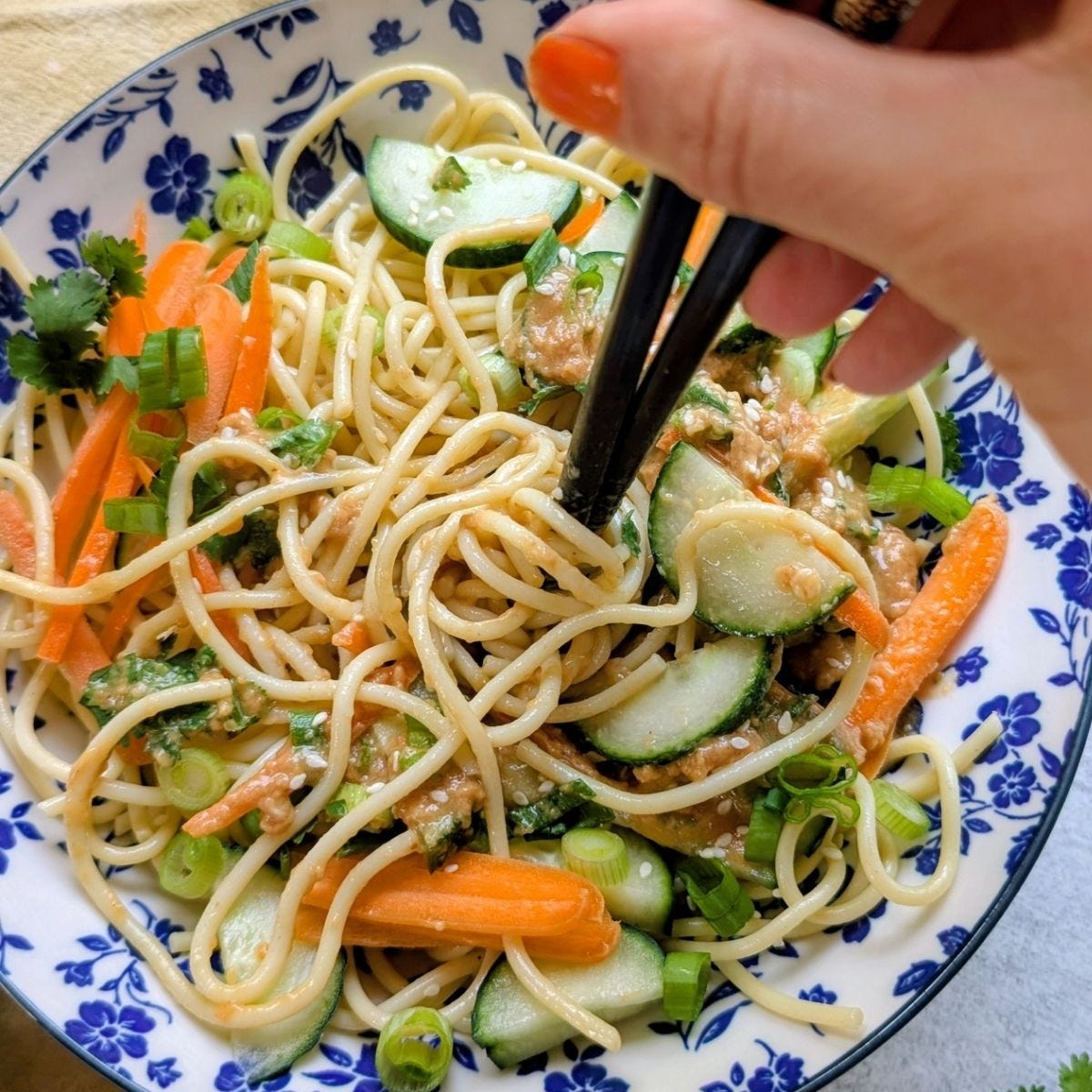 a hand twirling low salt noodle salad with chopsticks in a low salt peanut dressing