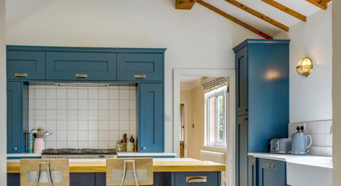 A kitchen with blue cabinets, white walls, wooden beams on the ceiling, and an island A kitchen with blue cabinets, white walls, wooden beams on the ceiling, and an island
