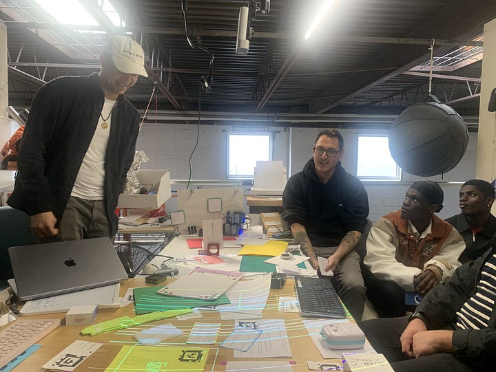 people around a table looking at programs all spread out & lit up by the projector above head