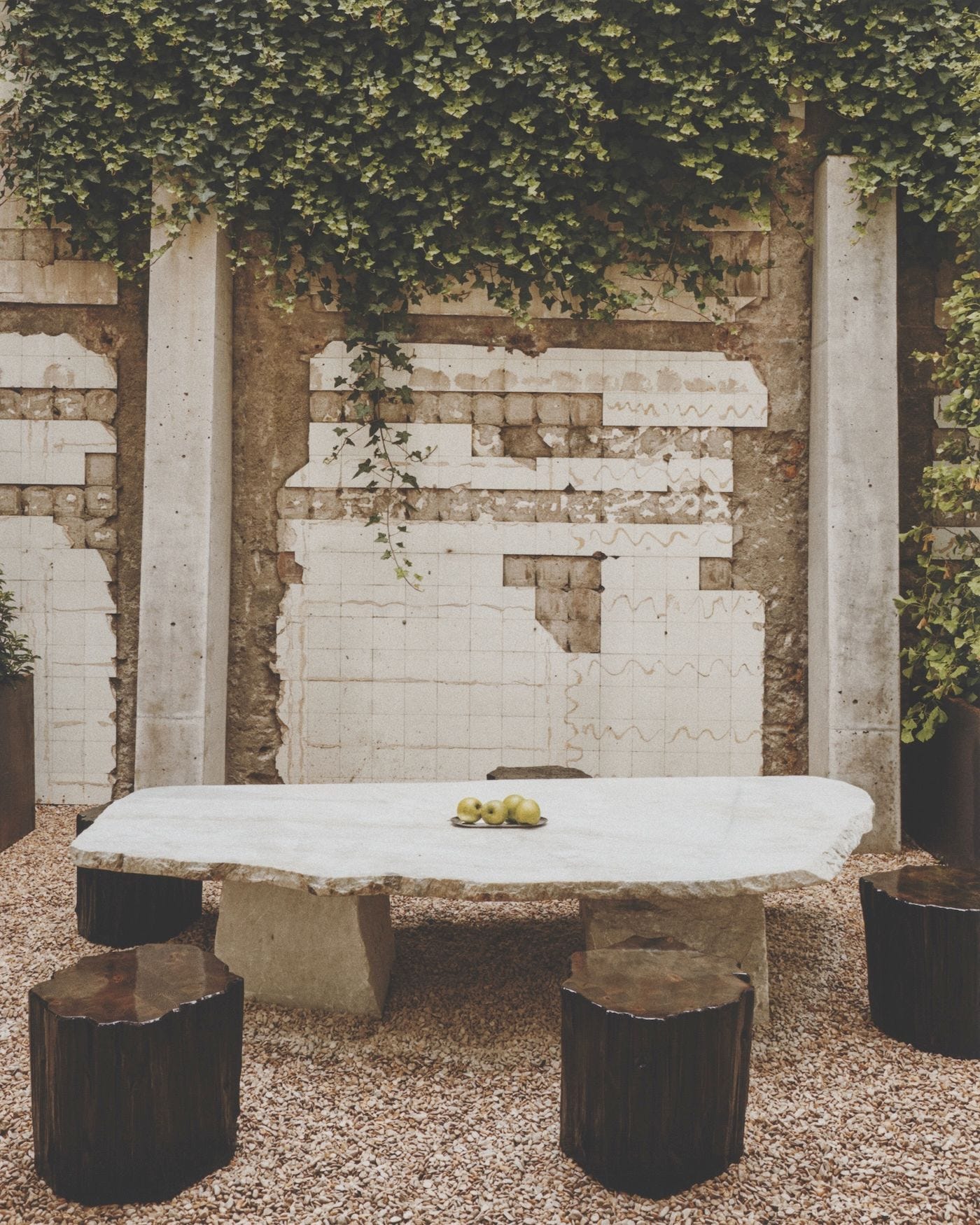 jardín con enredadera mesa blanca y taburetes negros.