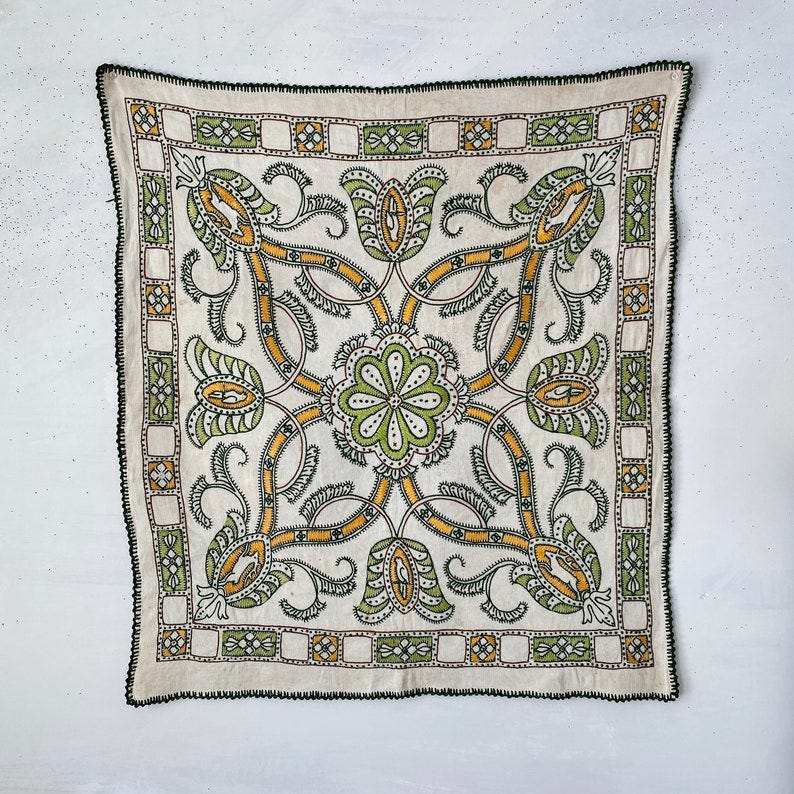 May include: A white fabric square with a black border and a repeating pattern of green and yellow floral designs.