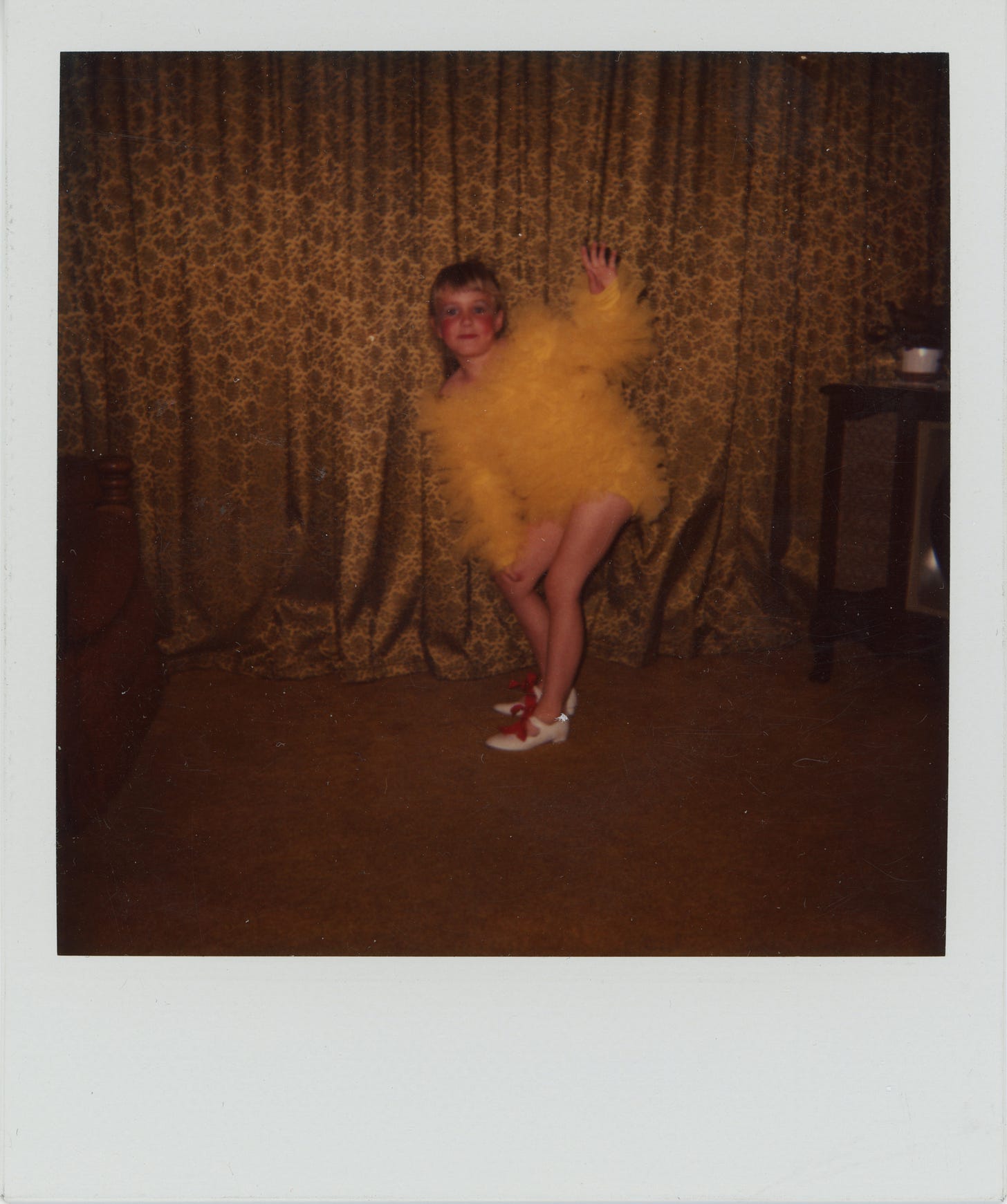 Karrie around 1980ish wearing a yellow tulle dance costume and tap shoes. She is posing with one arm in the air in a shot from the dance routine. She has lots of makeup on for the stage. 