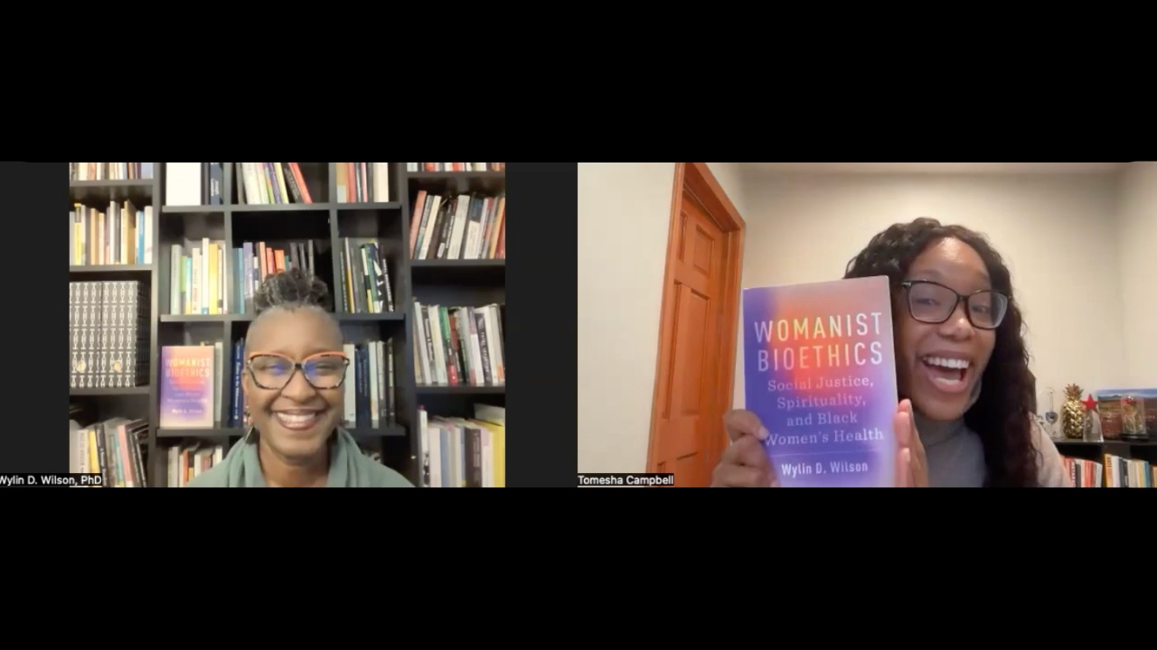 Split-screen video call showing two Black women smiling. One sits in front of a bookshelf, while the other holds up the book Womanist Bioethics: Social Justice, Spirituality, and Black Women’s Health during an interview.