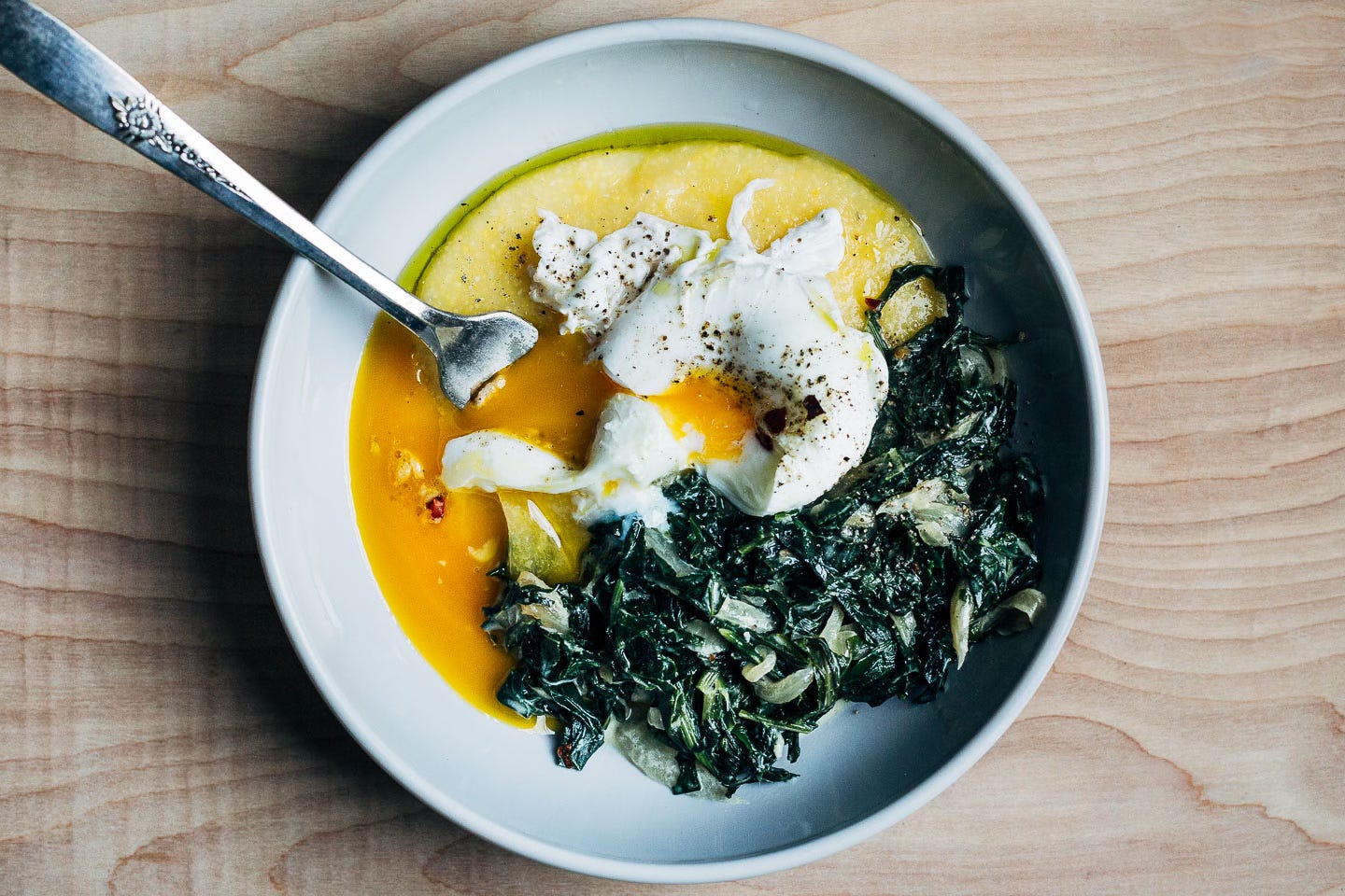 Creamed greens, polenta, and a runny poached egg in a bowl. 