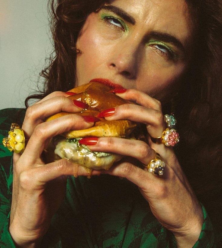 This may contain: a woman in green shirt eating a large sandwich