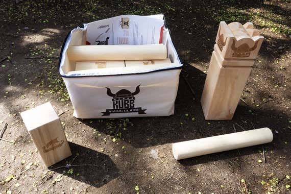 A kubb game set on the ground, including a carrying bag, wooden blocks, and a king piece with a crown design. A kubb game set on the ground, including a carrying bag, wooden blocks, and a king piece with a crown design.
