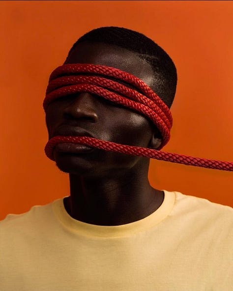 Three stylized studio portraits against vivid orange-red backgrounds: on the left, a person with long black hair covers another person’s eyes from behind; in the center, a person with red rope wrapped around their eyes and mouth; on the right, a person crouches while a high-heeled shoe presses against their open mouth, with a small pink bottle on the floor nearby.