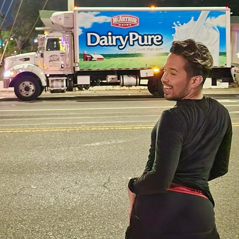 Ditzy Darry, a young man in a black long-sleeve shirt stands on the street at night, looking back over his shoulder with a laugh and his pants down, underwear out. A large MArthur Dairy DairyPure milk truck is visible in the background. Ditzy Darry, a young man in a black long-sleeve shirt stands on the street at night, looking back over his shoulder with a laugh and his pants down, underwear out. A large MArthur Dairy DairyPure milk truck is visible in the background.