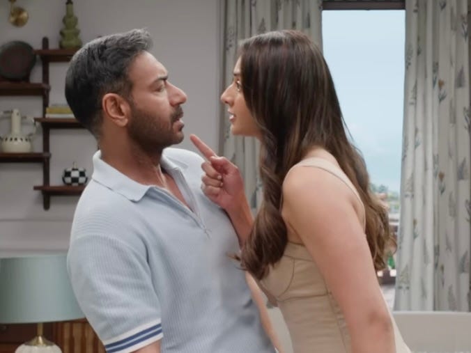 A still from Hindi film, ‘De De Pyaar De 2 (2025)’. Ashish (Ajay Devgn) and Ayesha (Rakul Preet) stand very close to each other in a tense, emotionally charged moment. Ayesha leans forward, pointing a finger at Ashish’s chest as she speaks intensely, while Ashish leans slightly back, looking at her with a mix of surprise and concern. They are indoors in a well-lit living room with shelves and a window in the background.
