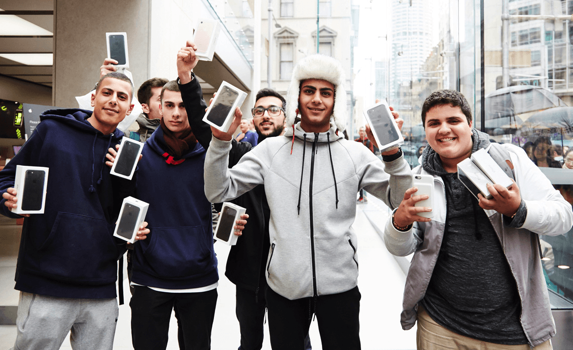 Group of excited Apple fans holding iPhones outside a flagship store