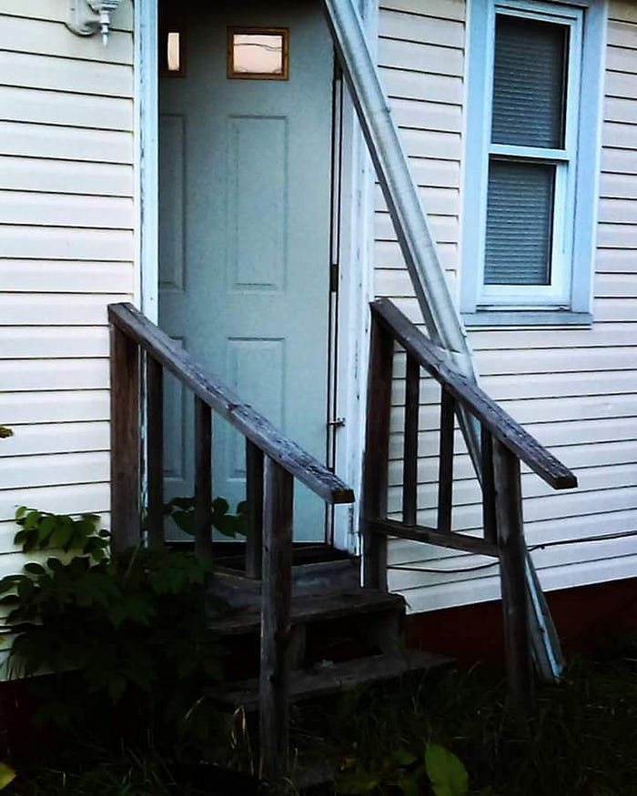 Grainy picture of a run-down doorway of an abandoned house.