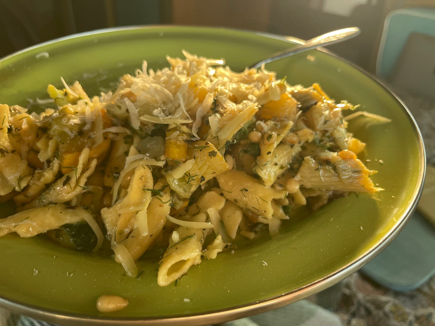 a plate of pasta, cooked zucchini and flakes of fresh cheese on a metal plate