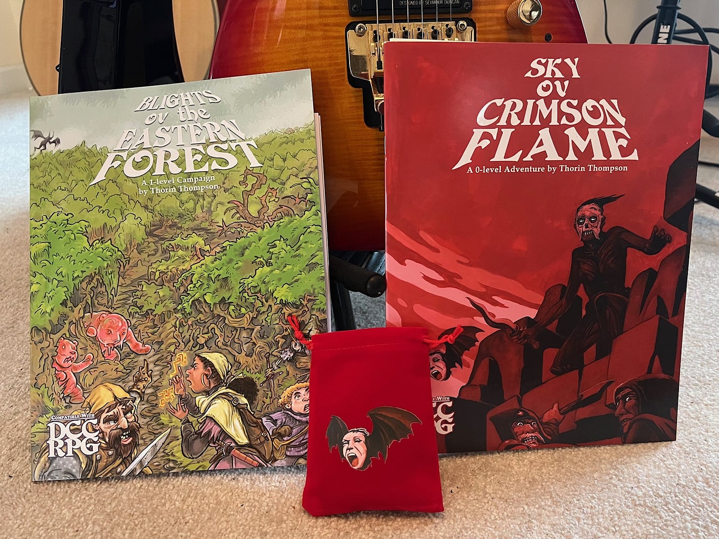 Two TTRPG paperbacks and a red dice bag in front of an electric guitar.