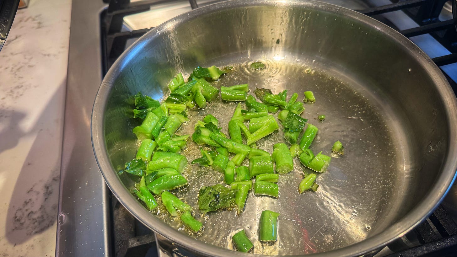 Chopped gai lan stems in hot olive oil in a saute pan