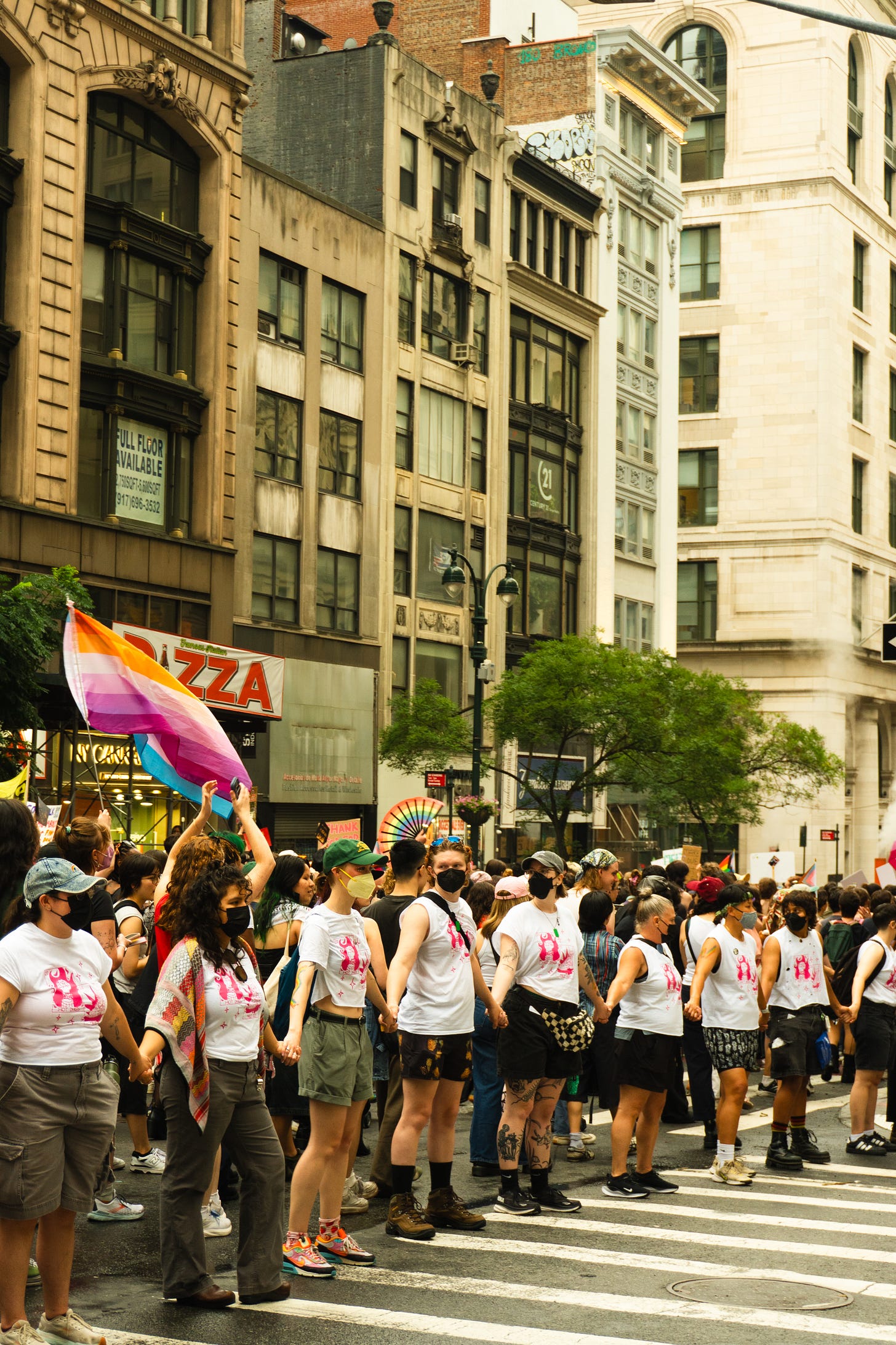 Dyke March Marshalls hold hands on a sidewalk while wearing masks.