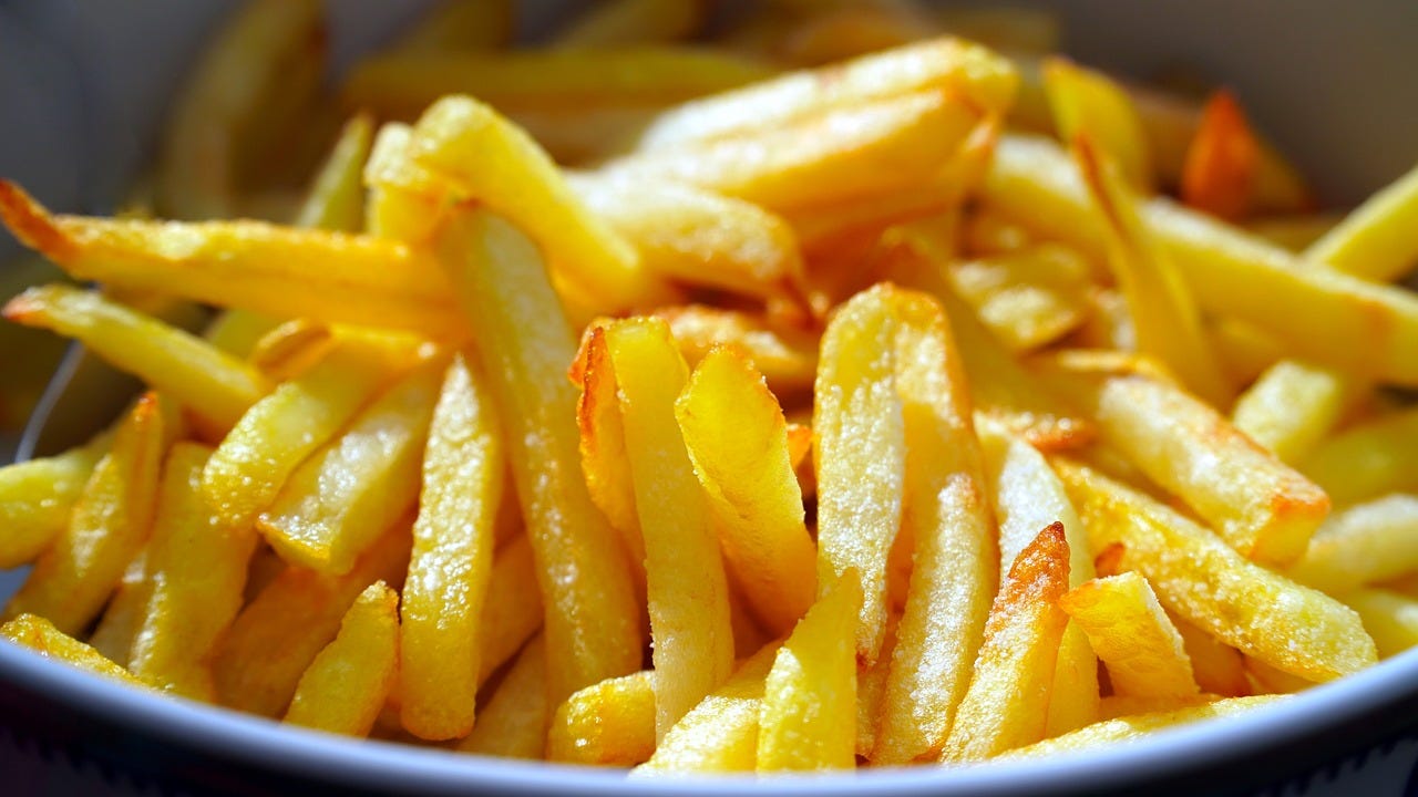 Golden, crispy French fries in a bowl, under bright lighting, highlighting their texture and inviting appearance. No text visible.