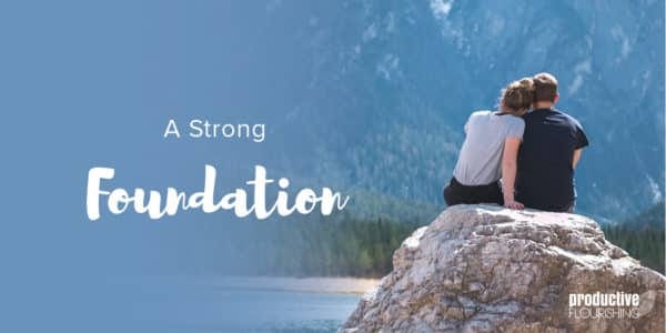 Two people face the water while sitting on a rock; they lean on each other. Text Overlay: A Strong Foundation Two people face the water while sitting on a rock; they lean on each other. Text Overlay: A Strong Foundation
