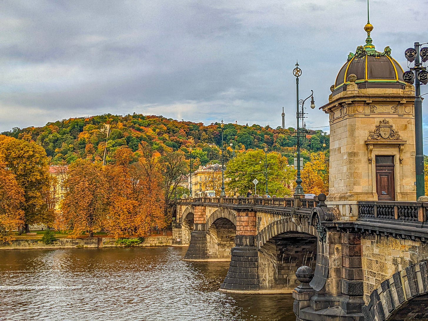 One of Prague's beautiful sandstone bridges with colorful fall trees behind it. 