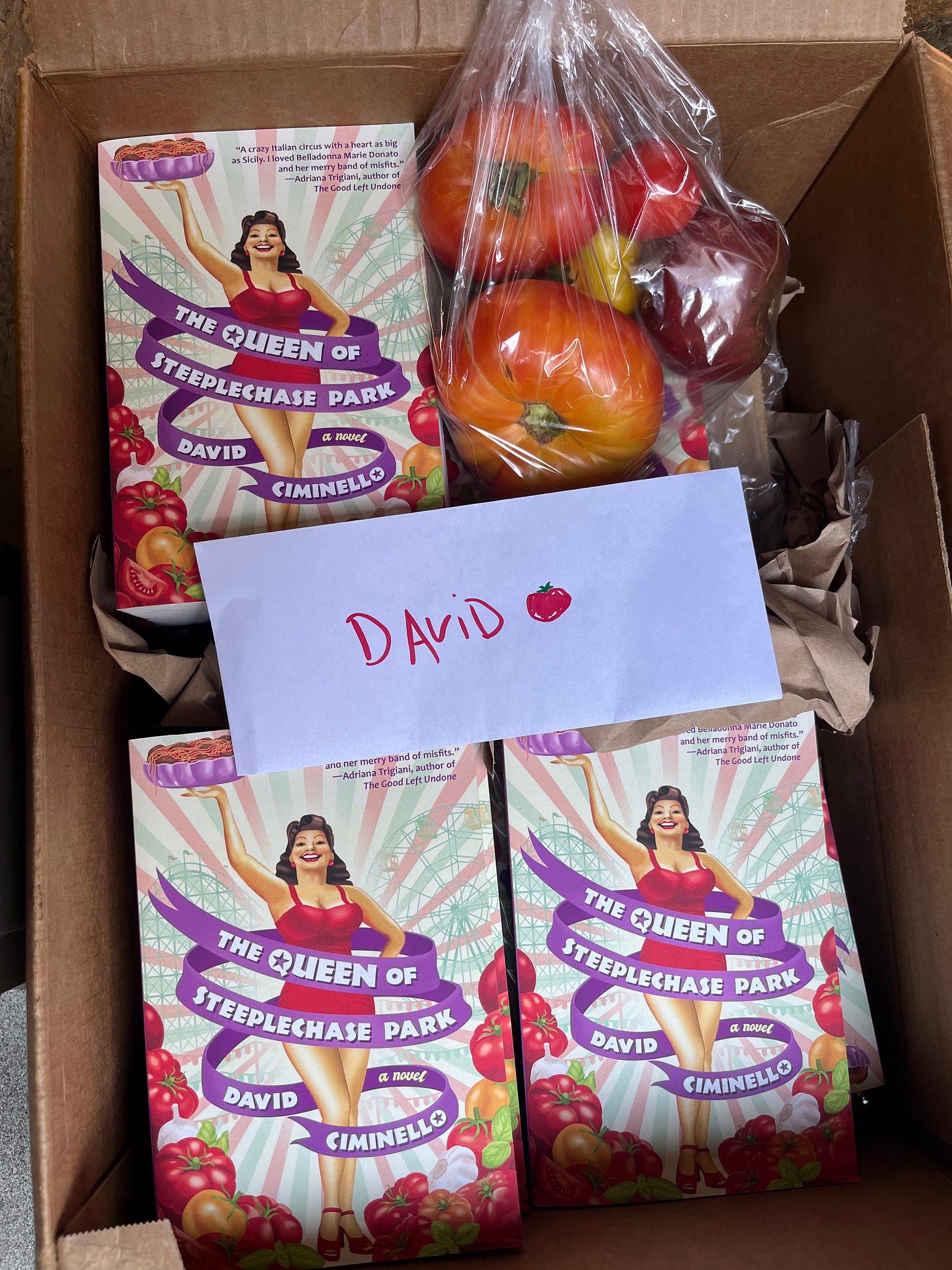 A box of books with a young lady in a red bathing costume on the cover, plus a note that says DAVID and a bag of heirloom tomatoes. A box of books with a young lady in a red bathing costume on the cover, plus a note that says DAVID and a bag of heirloom tomatoes.