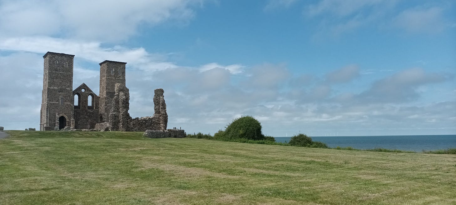 Reculver Towers, two church towers on a grassy headland with the sea and blue sky in the background