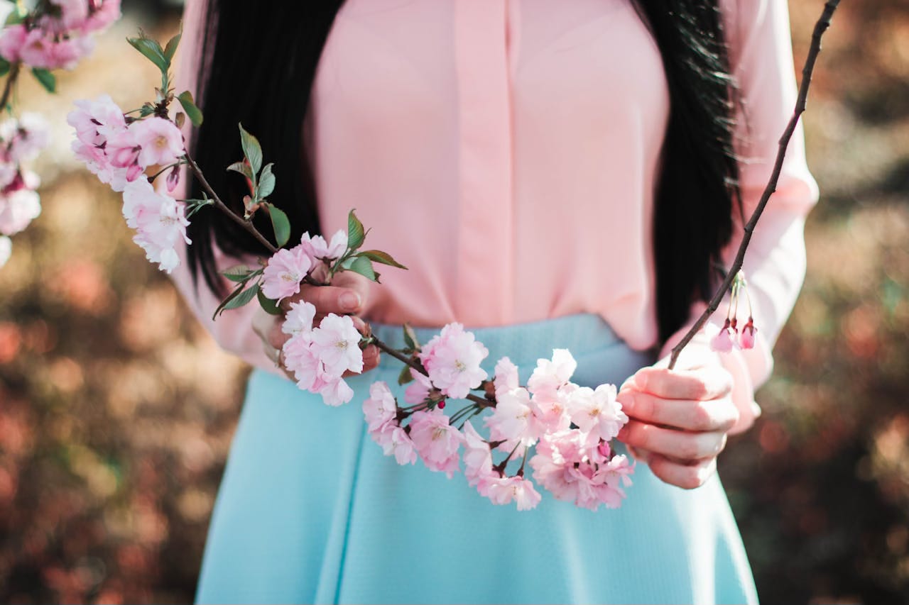 A cropped image of a woman in a pink shirt and turqoise skirt holding a branch of pink flowers A cropped image of a woman in a pink shirt and turqoise skirt holding a branch of pink flowers