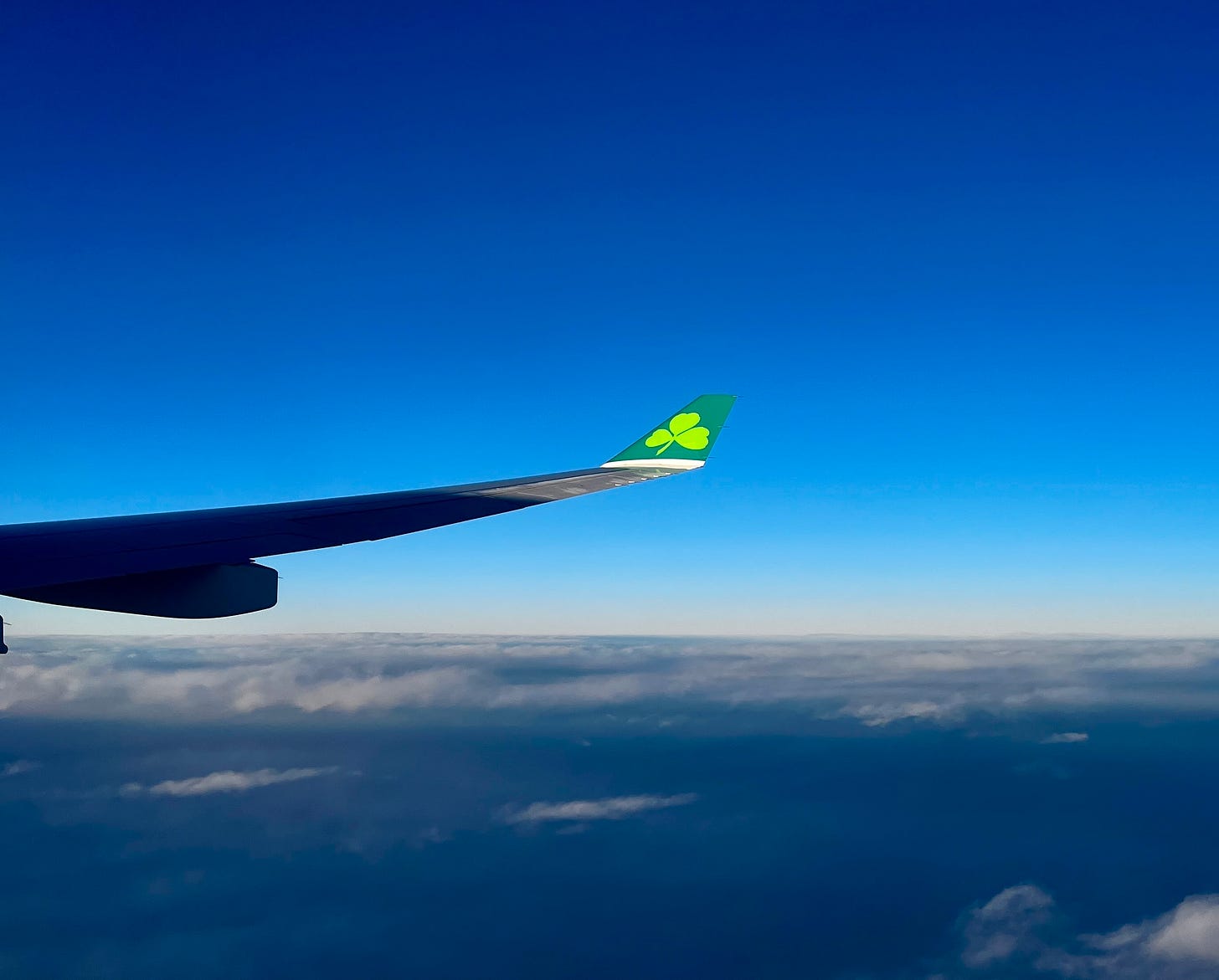 Airplane wing with shamrock logo above clouds and deep blue sky. Airplane wing with shamrock logo above clouds and deep blue sky.