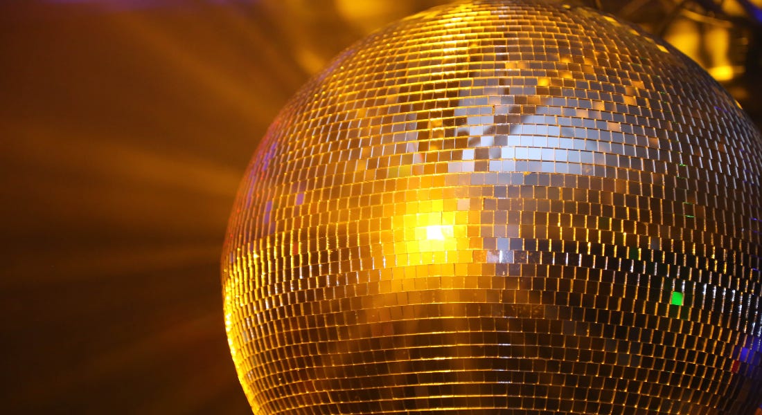 A silver disco ball with a gold light shining on it