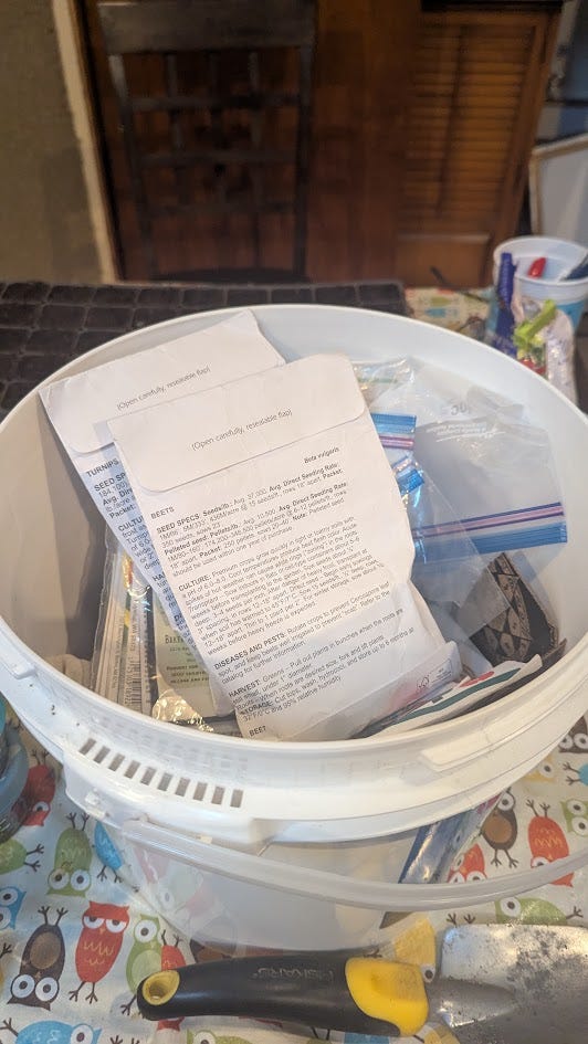 A white plastic bucket with a lid, the inside contains many seed packets in plastic bags.