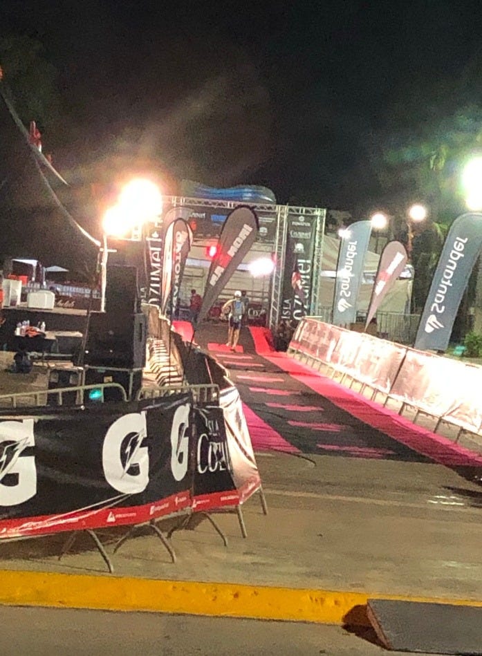 Ironman Cozumel finish line with a lone runner going under the banner in the dark evening