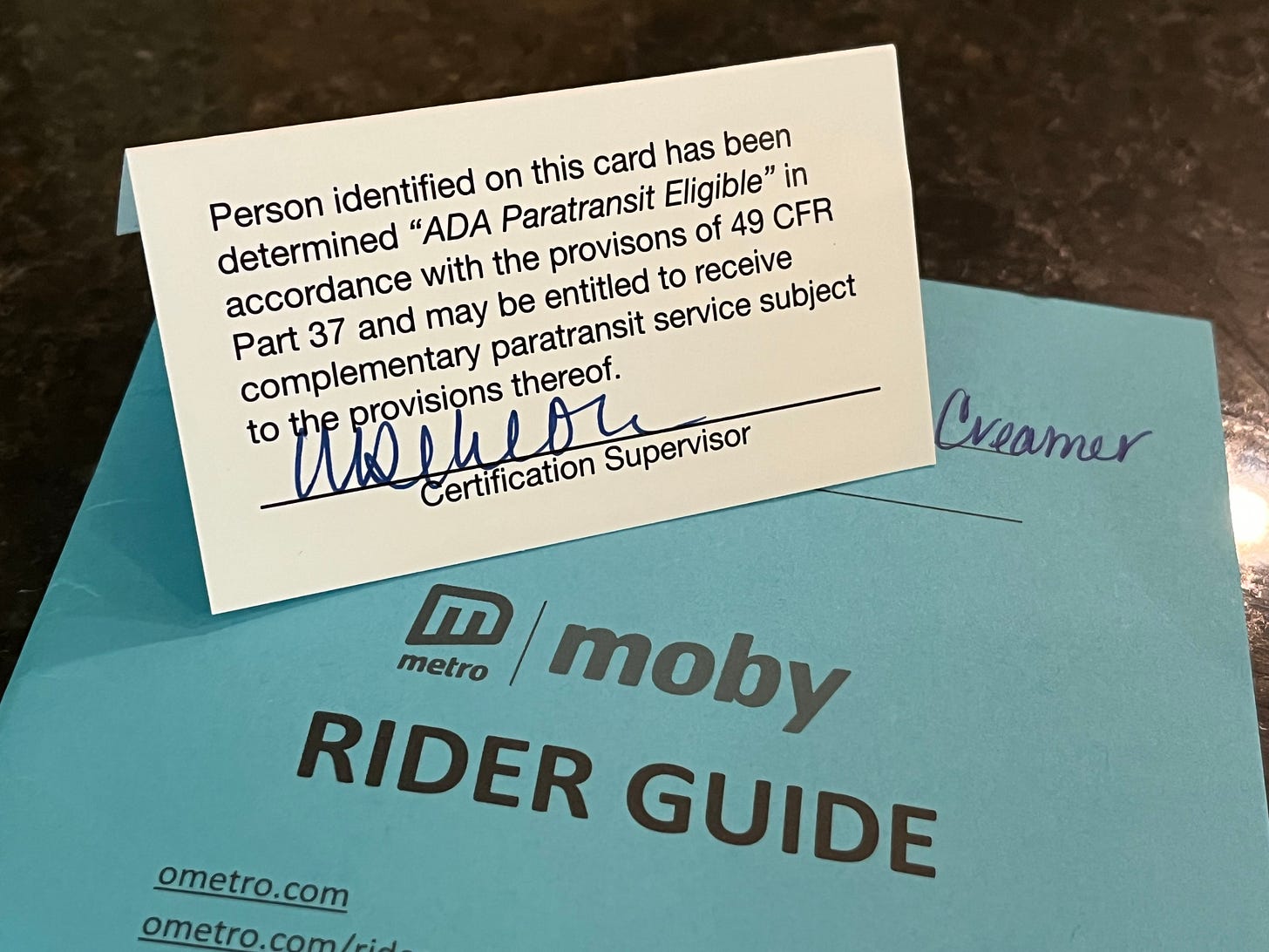 Blue cover of paratransit riders guide and a white membership card stating that the person identified this card has been determined “ADA paratransit eligible”