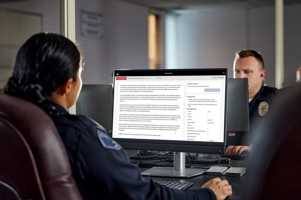 A photo of two police officers facing each other with their computer monitors in between, and the monitor of the officer closest to the camera has the Axon Draft One platform displayed on its screen.
