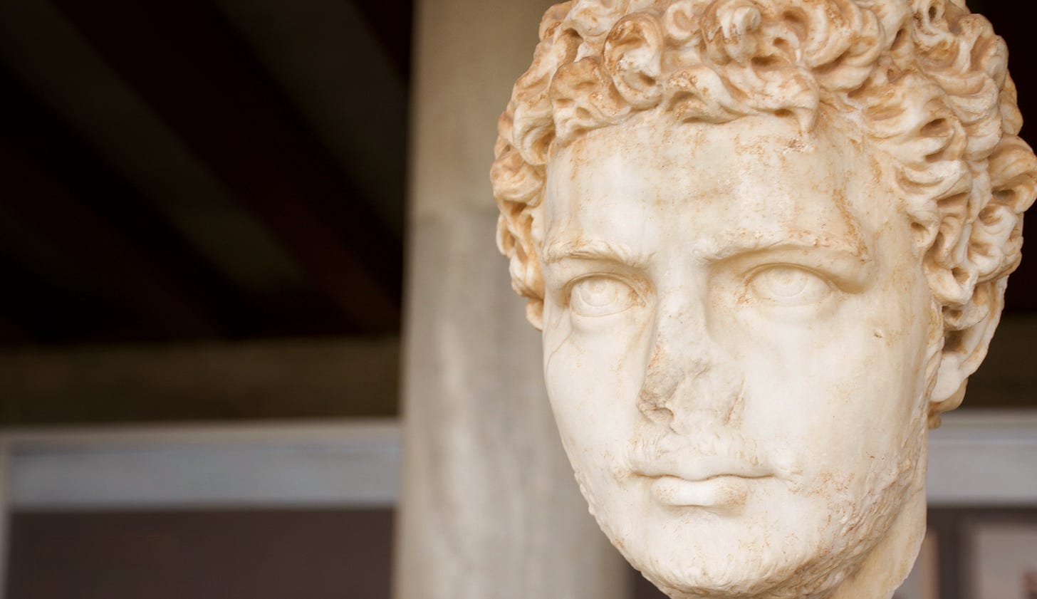 Photograph of a carved marble head in the Stoa of Attalos at the Ancient Agora in Athens, Greece. The sculpture looks down a long colonnade, symbolising endurance, craft and human presence in contrast to disposable, automated content.