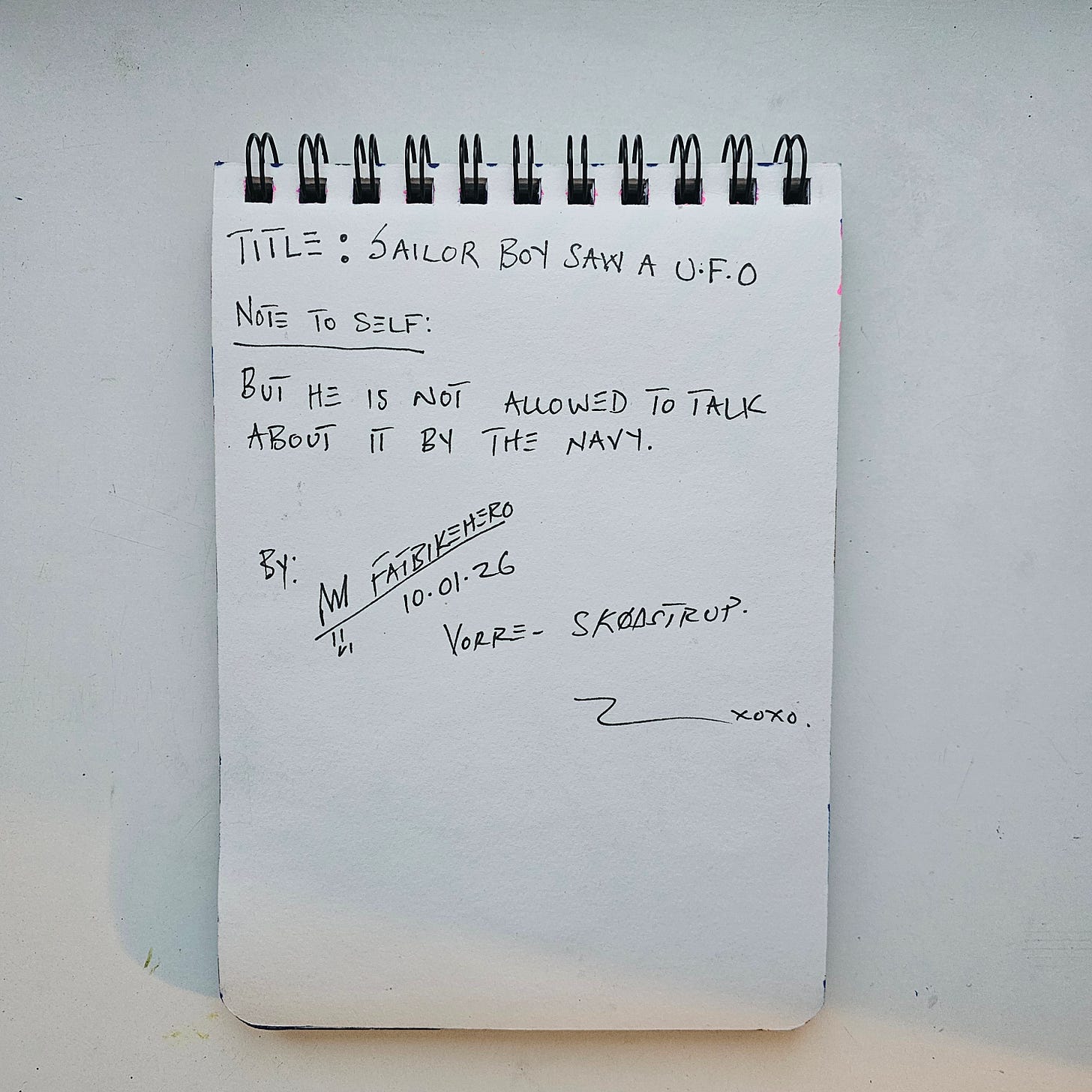 Alt Text: The back of a sketchbook page showing handwritten text in black ink. It reads "TITLE: SAILOR BOY SAW A U.F.O" followed by "NOTE TO SELF: BUT HE IS NOT ALLOWED TO TALK ABOUT IT BY THE NAVY." It is signed "BY: FATBIKEHERO," dated "10.01.26," and located "VORRE - SKØDSTRUP."
