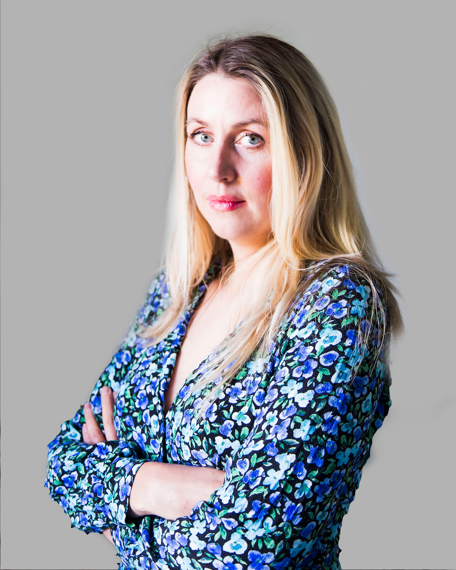 A photo of the writer Emily Jupp, with her arms folded, in a blue flowery dress