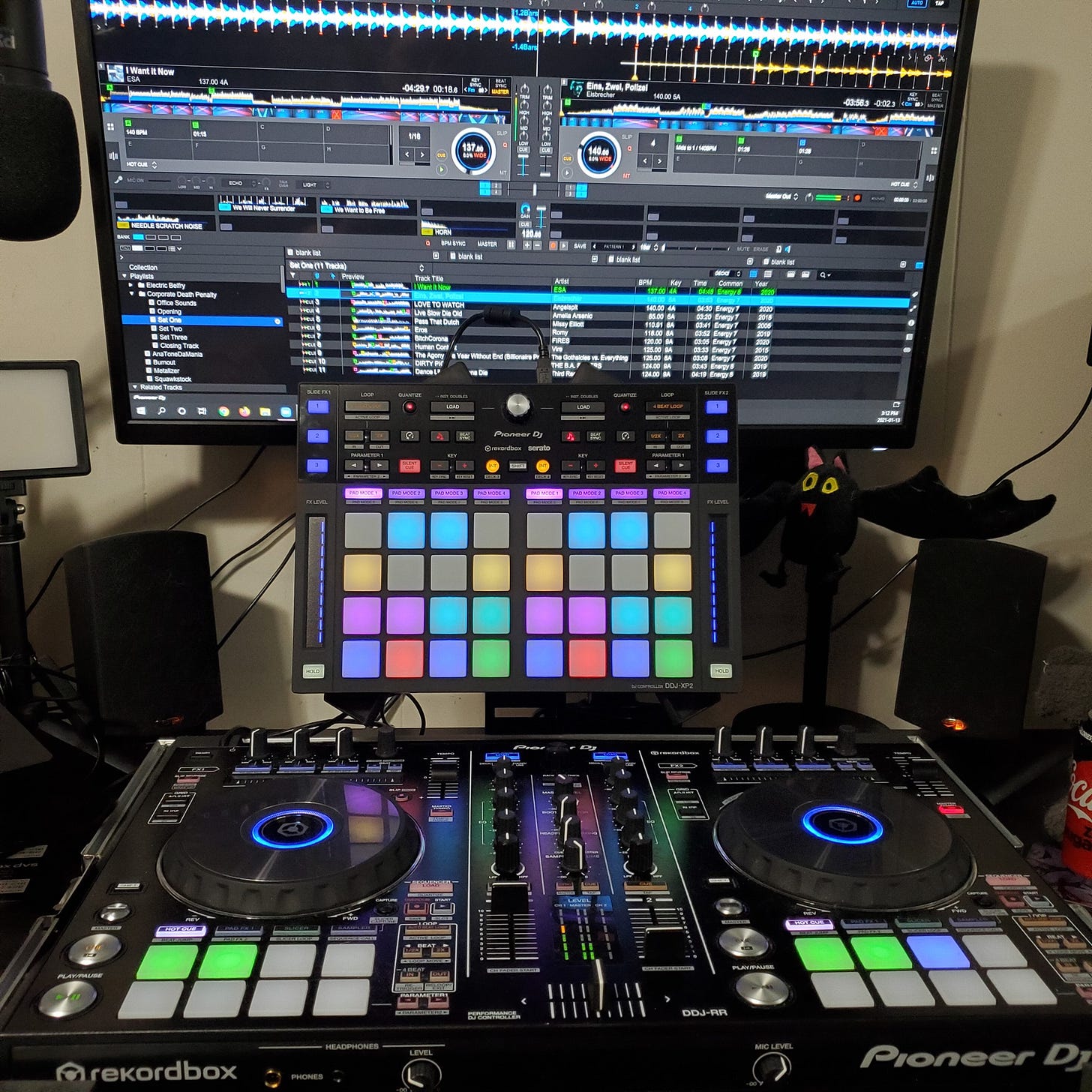 A DJ controller in the foreground, with another subcontroller just behind it. On the screen Rekordbox DJ software is open.