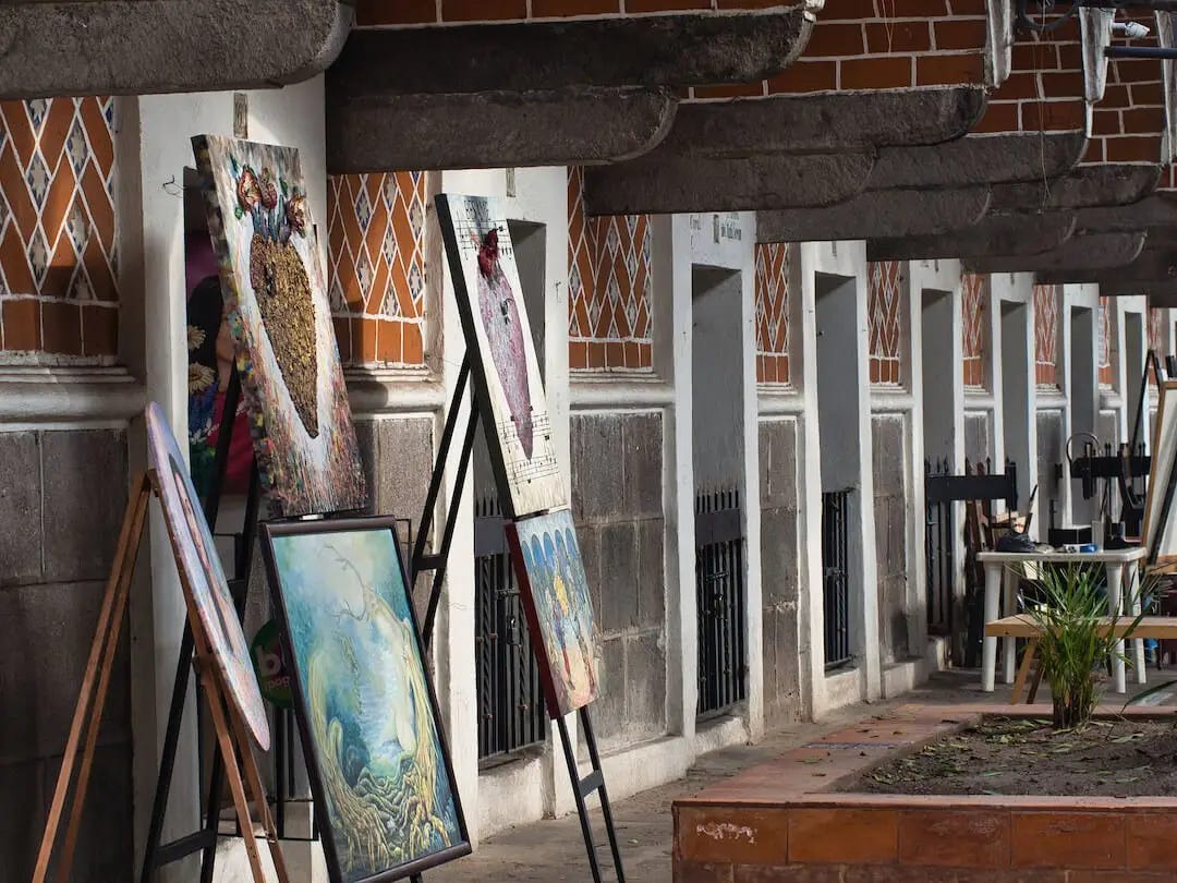 A row of small red-tiled studios with paintings on display