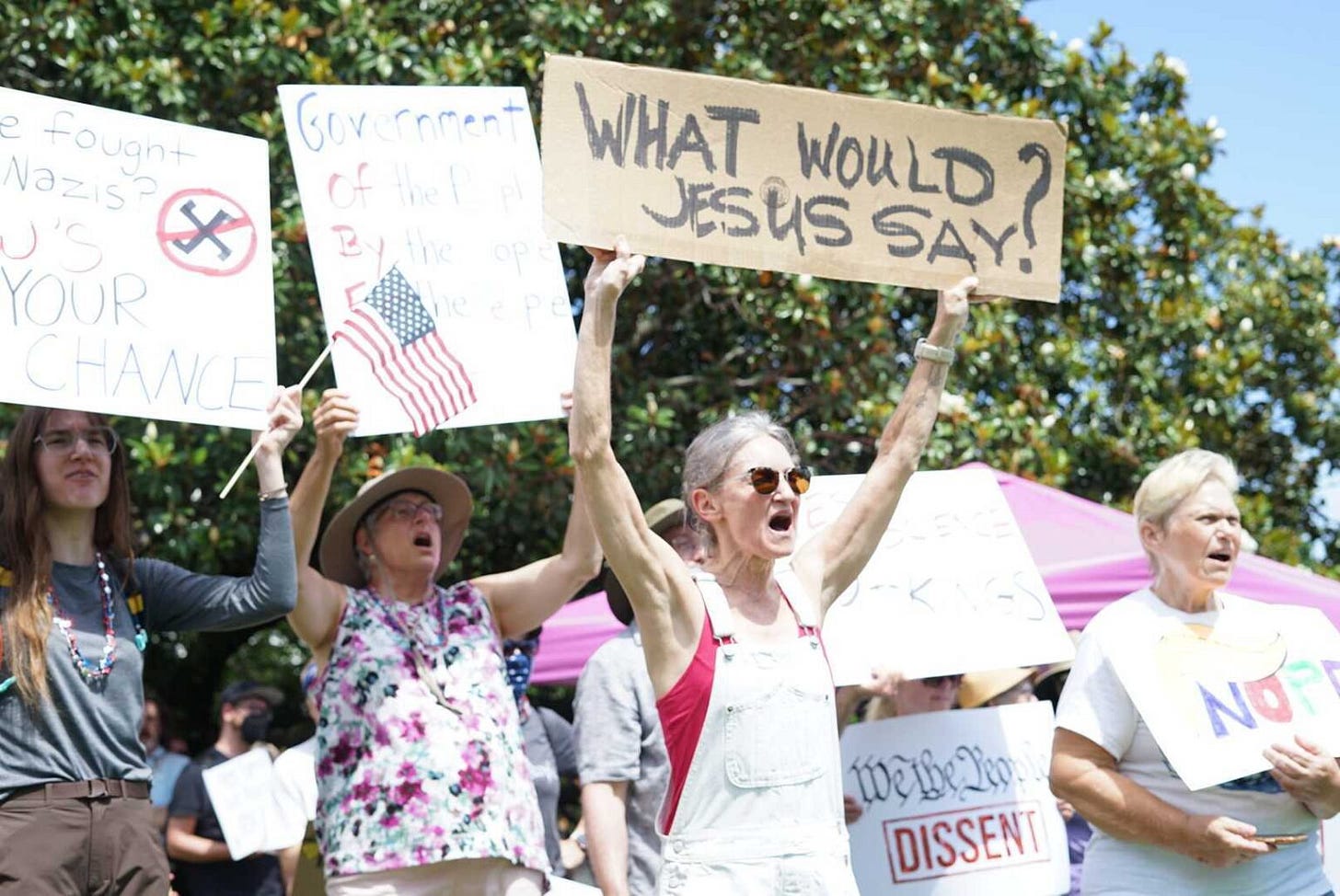 A woman holds a sign that says "what would Jesus do" at a protest.