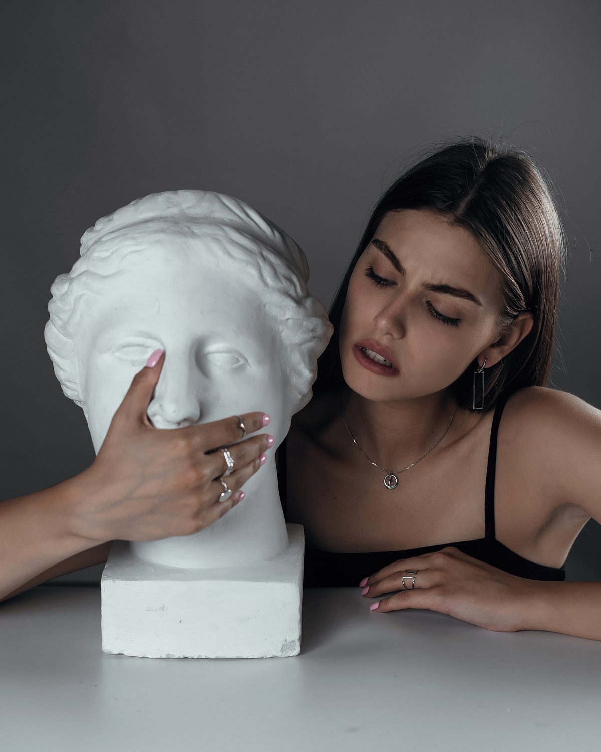 A woman next to a roman statue head. She is covering the statue’s mouth.
