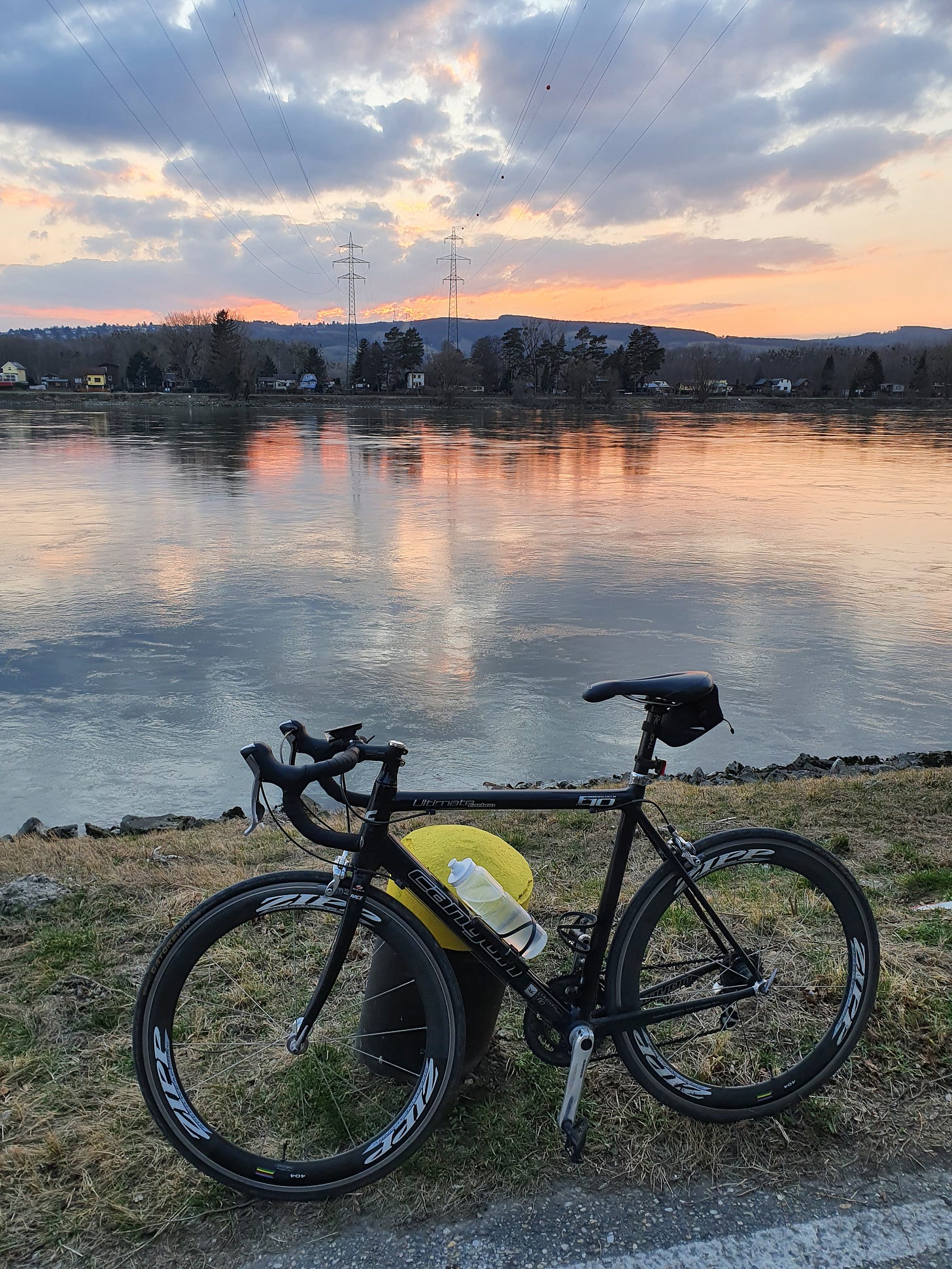 Black roadbike leaned against a post a sunset on the river