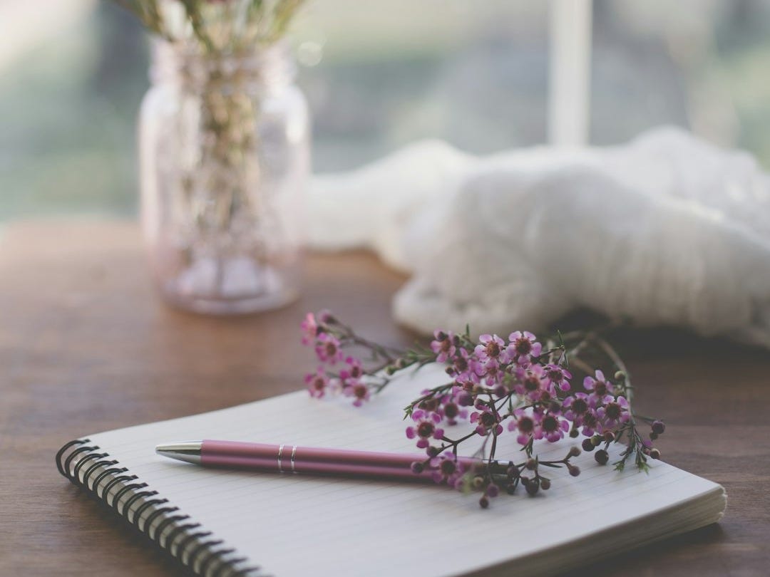 shallow focus photo of purple flowers on white spiral notebook