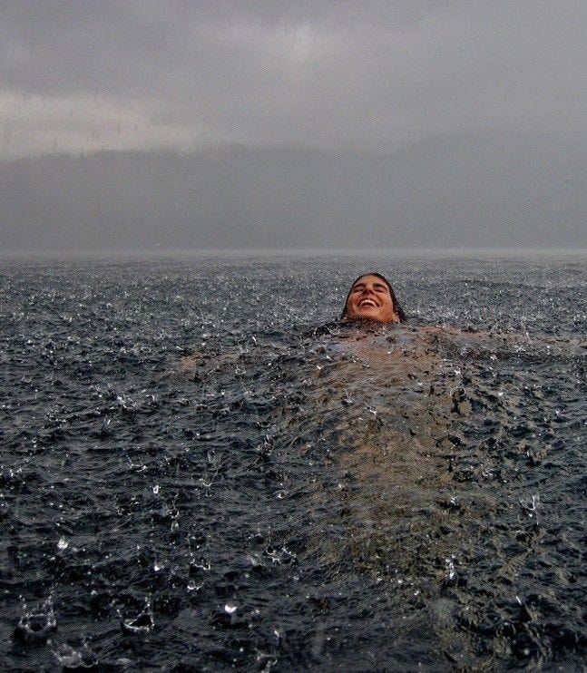 This may contain: a woman swimming in the ocean with her head above the water's surface and dark clouds overhead