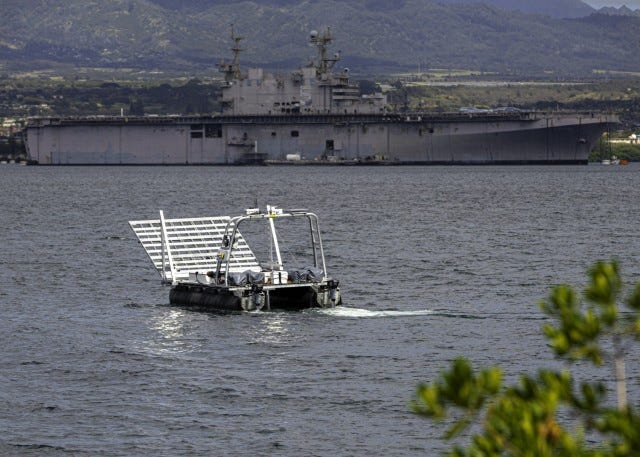 An unmanned surface vessel (USV) maneuvers through the water with the USS Peleliu in the background during a rehearsal for Project Convergence - Capstone 5 (PC-C5) at Pearl Harbor, Hawaii, in April 2025. During the PC-C5 experiment, USVs completed...