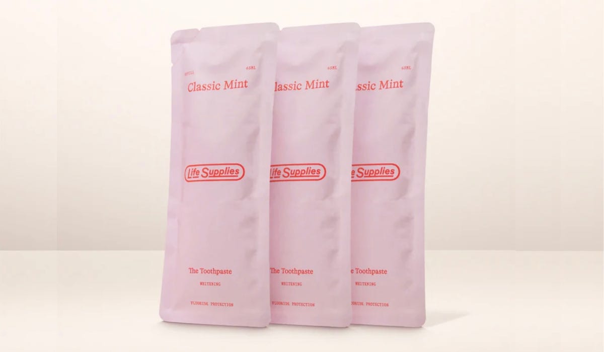 Three packs of Life Supplies toothpaste in pink pouches, against a neutral plain background.