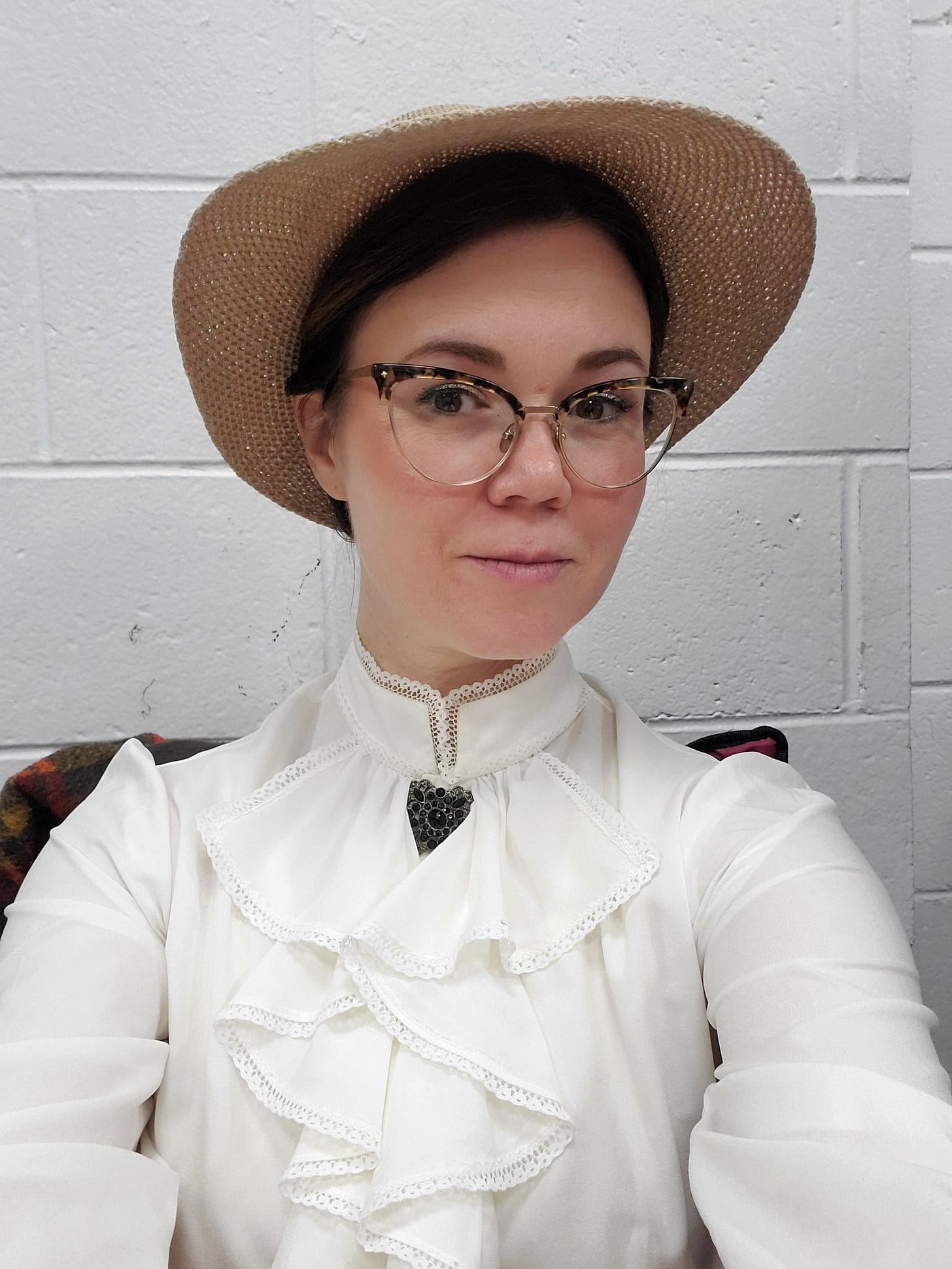 White woman in a straw hat and white Victorian style blouse, staring at the camera