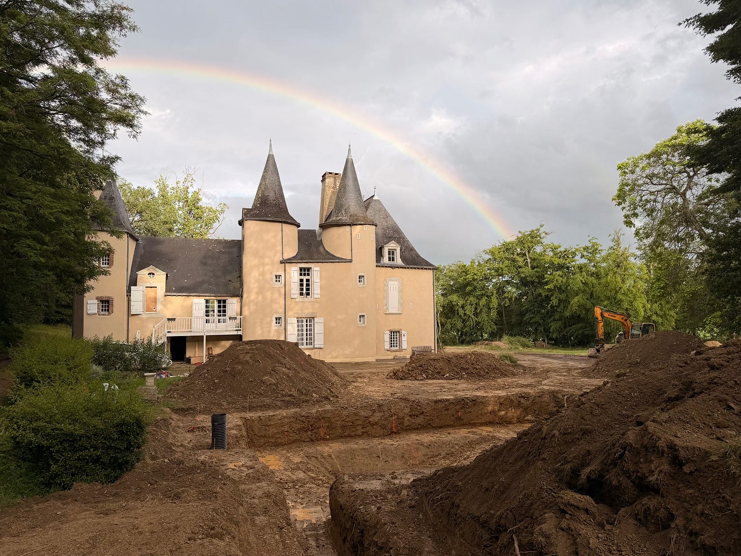 A rainbow arcs over a turreted château under a grey storm sky, with mounds of excavated earth, an open trench and a yellow digger in the foreground. A rainbow arcs over a turreted château under a grey storm sky, with mounds of excavated earth, an open trench and a yellow digger in the foreground.
