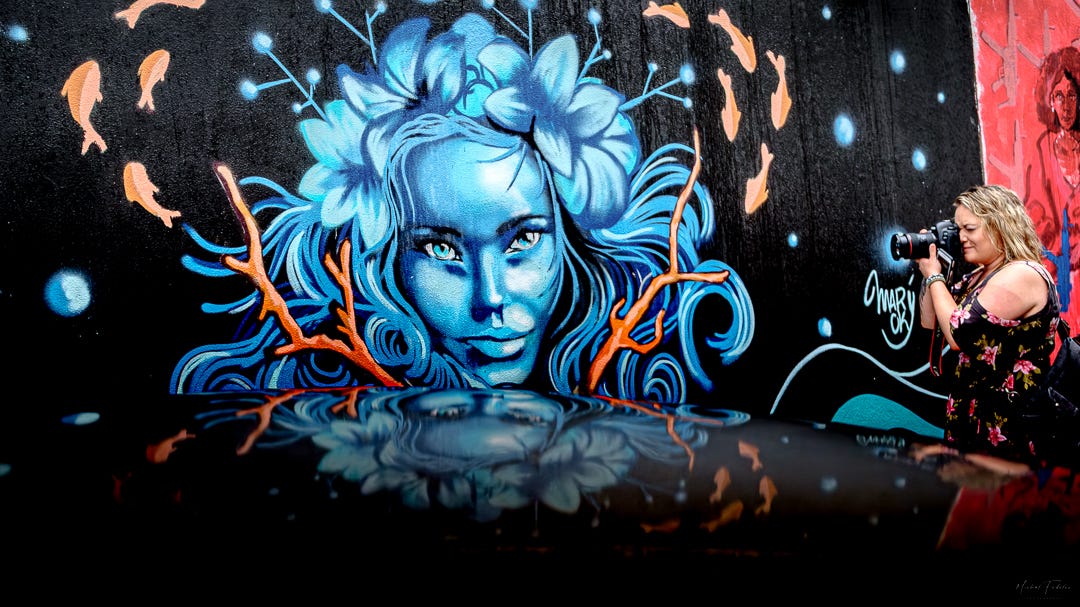 A striking mural depicting a woman's face, with a female photographer on the side