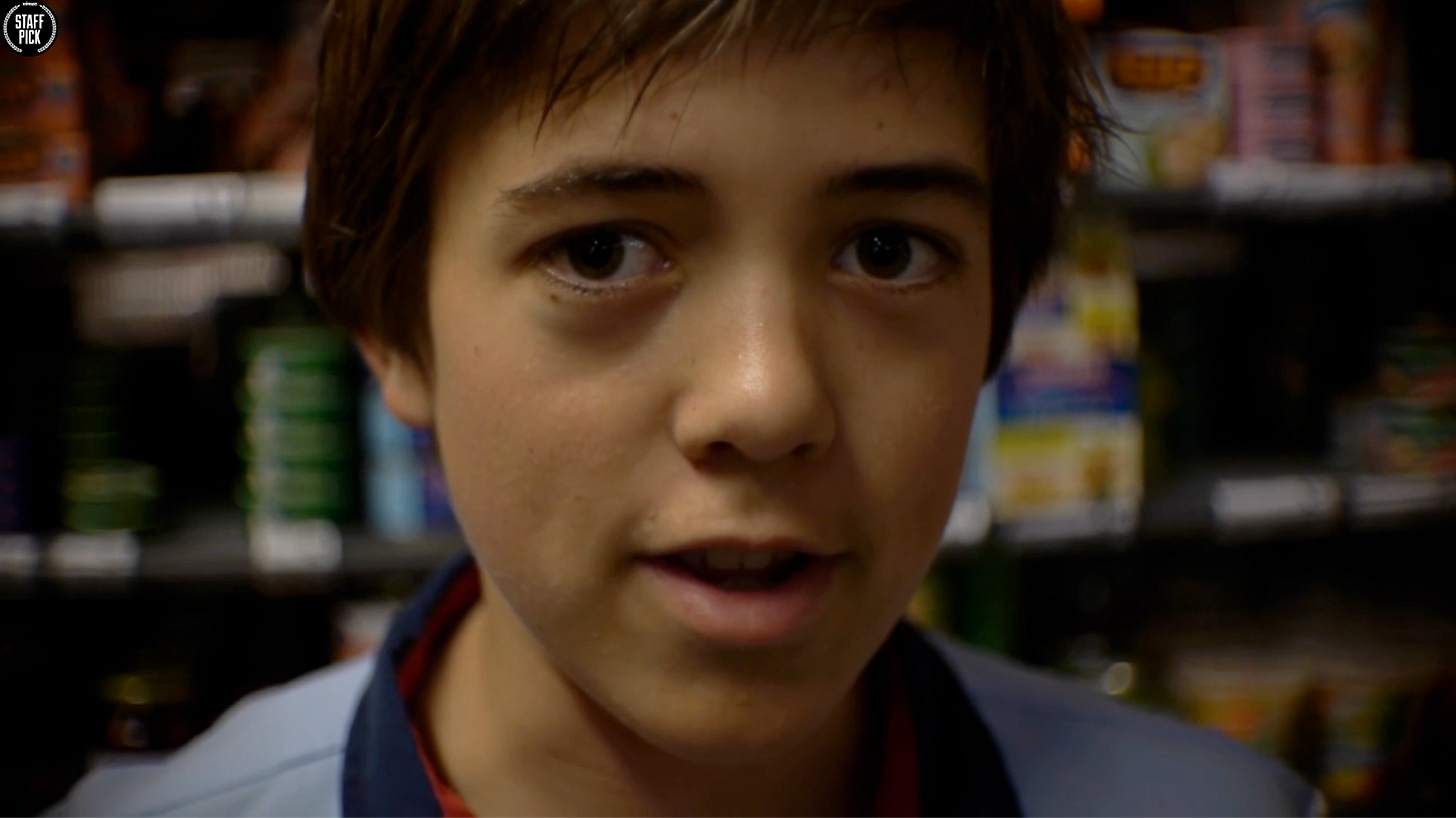 Close-up portrait of a brown-skinned teenage boy with dark brown hair wearing a striped shirt, smiling at the camera in what appears to be a store.